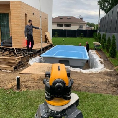 Установка композитного бассейна с нивелиром у современного дома и газона